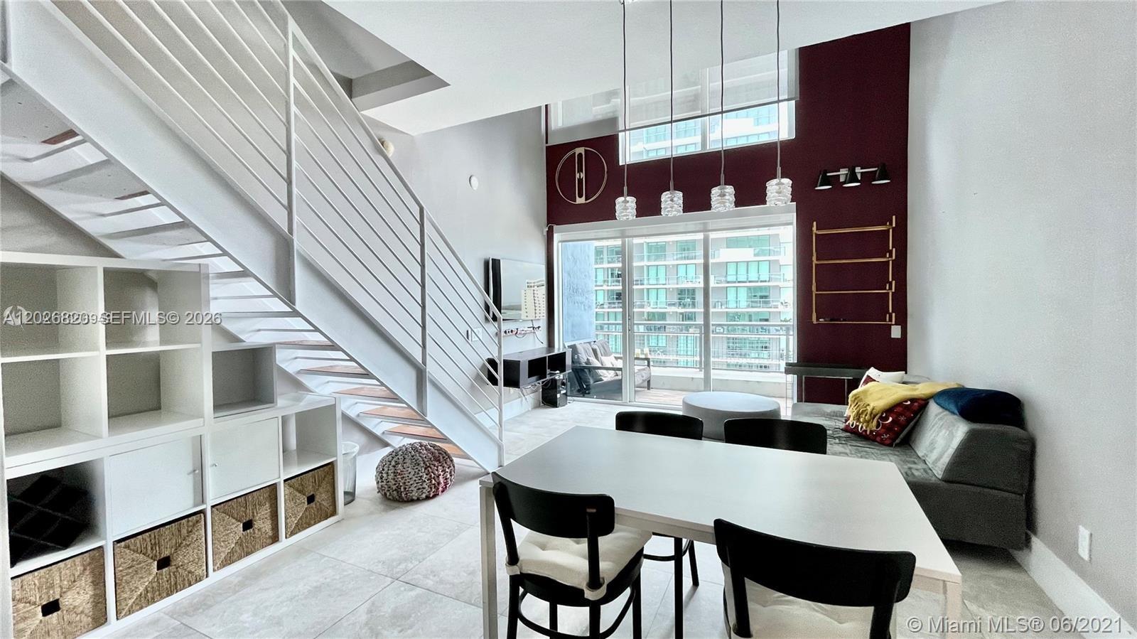 A modern living and dining area features a white staircase, high ceilings, and floor-to-ceiling windows — 60 SW 13th St # 2002, Miami FL 33130, MIAMI, FL