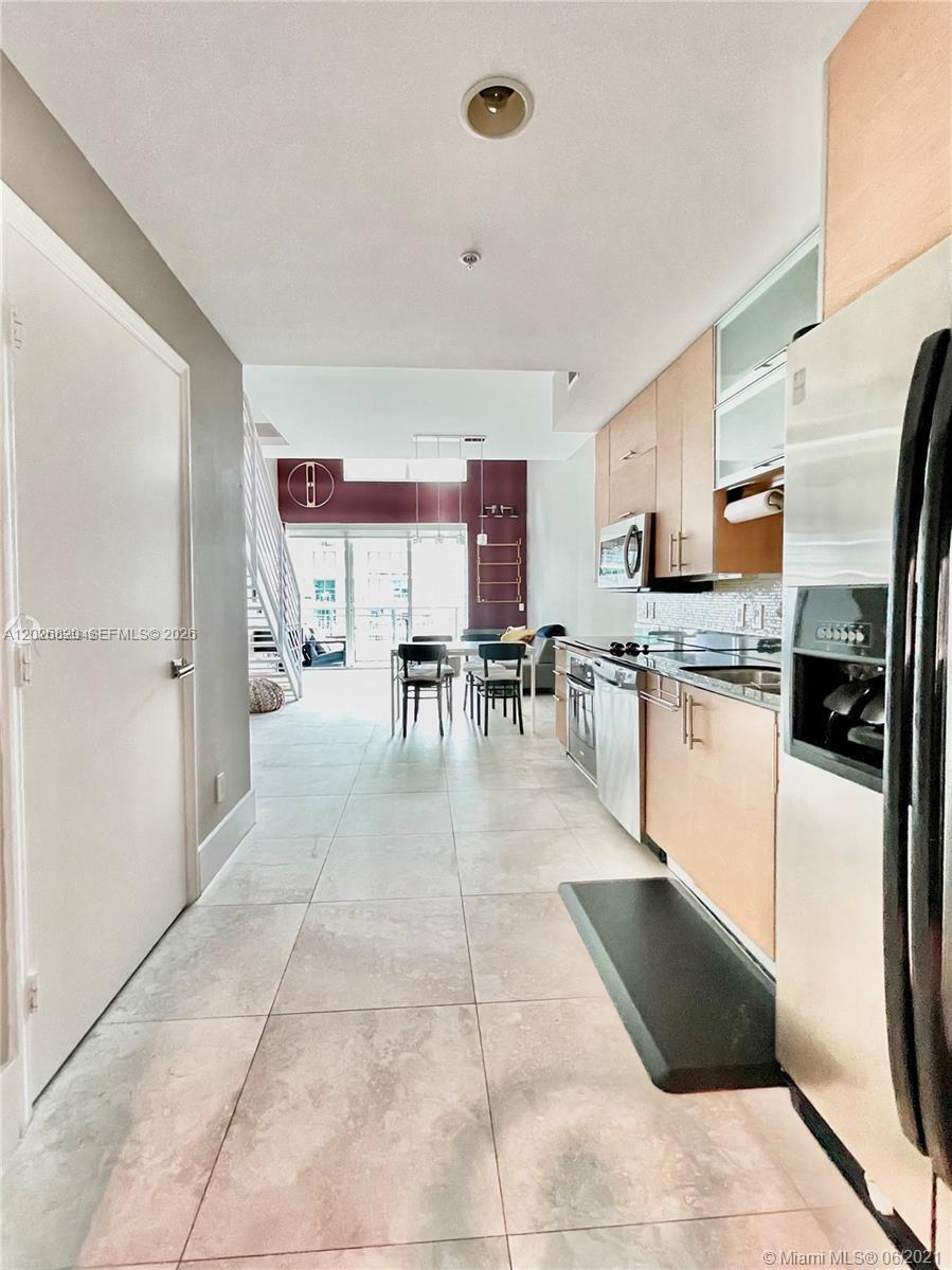 A galley kitchen with light wood cabinets leads to an open dining and living area — 60 SW 13th St # 2002, Miami FL 33130, MIAMI, FL