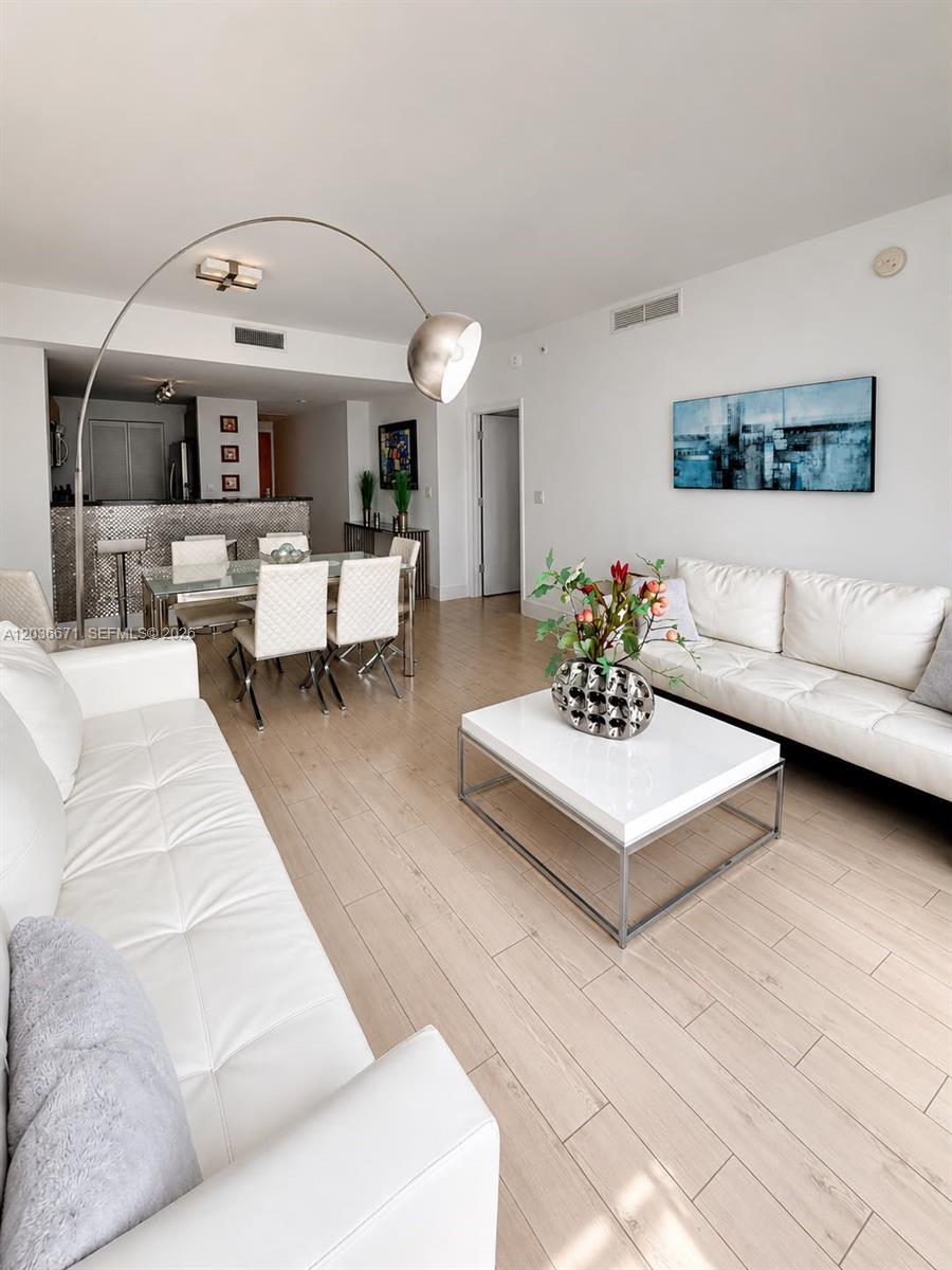 A modern living and dining area features white leather sofas, a glass table, and light flooring — 253 NE 2nd St # 3004, Miami FL 33132, MIAMI, FL