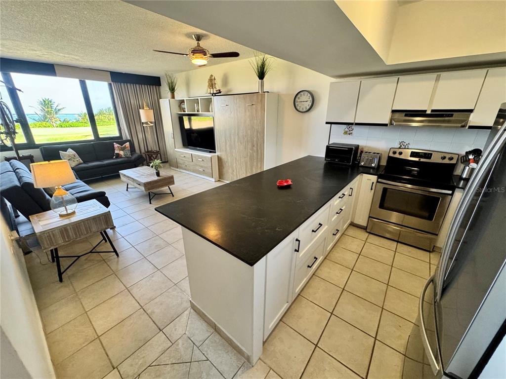 An open-concept kitchen with a dark island overlooks a living area with ocean views — 222 BEACH VILLAGE UNIT 222, HUMACAO, PR