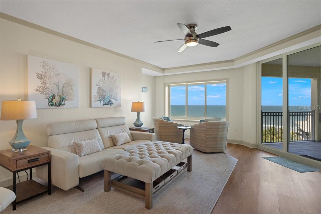 A living room features a white sofa, tufted ottoman, and large windows overlooking the ocean — 200 OCEAN CREST DRIVE UNIT 713, PALM COAST, FL