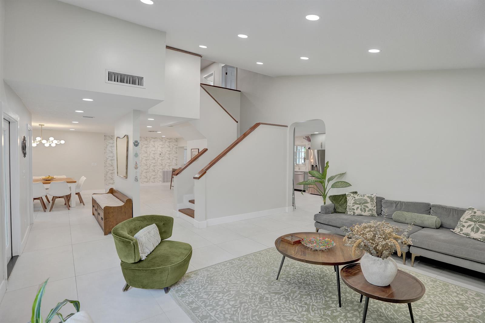 A bright living room features a grey sectional, green armchair, and a wooden staircase — 12213 Melissa Way, Cooper City FL 33026, COOPER CITY, FL