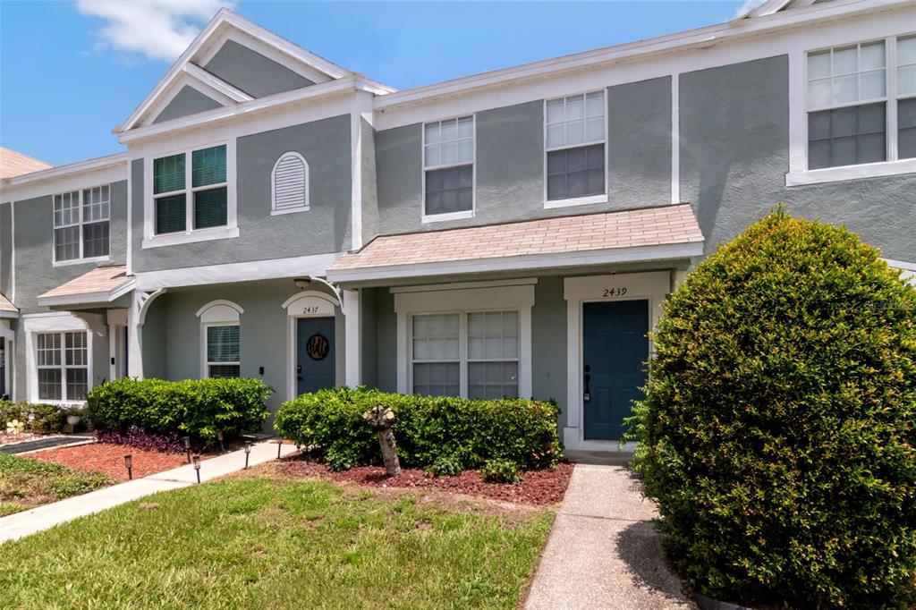 A two-story townhouse exterior features gray stucco siding, dark blue doors, and landscaped front bushes — 2439 LAKE WOODBERRY CIRCLE, BRANDON, FL