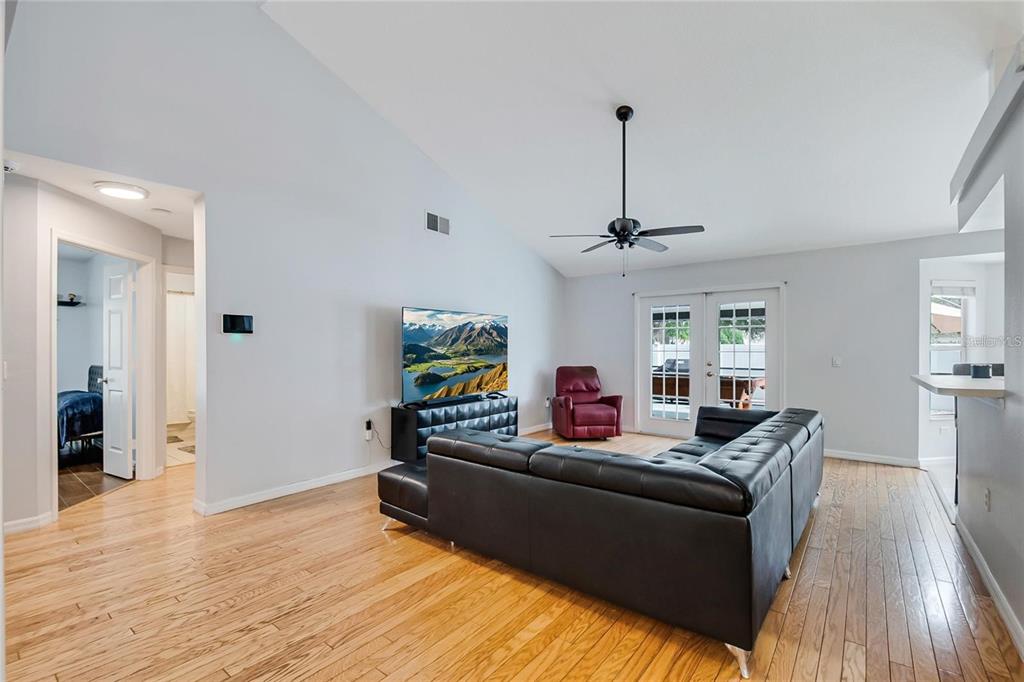 A living room features hardwood floors, a black sectional sofa, a television, and glass doors — 2305 JESSICA LANE, KISSIMMEE, FL