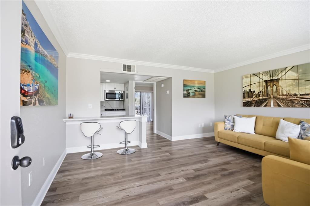 A living room with wood-look flooring, a breakfast bar with two stools, and a yellow sofa — 127 OYSTER BAY CIRCLE UNIT 110, ALTAMONTE SPRINGS, FL