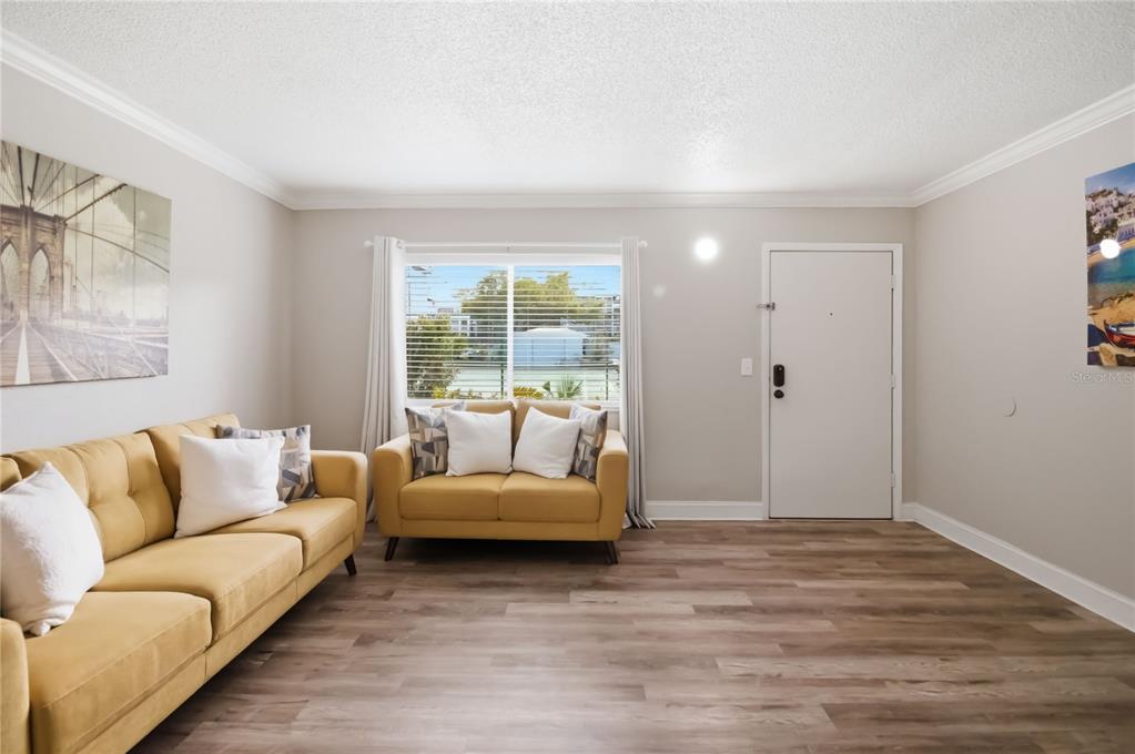 A living room features two yellow sofas, light wood-look flooring, and a white entry door — 127 OYSTER BAY CIRCLE UNIT 110, ALTAMONTE SPRINGS, FL