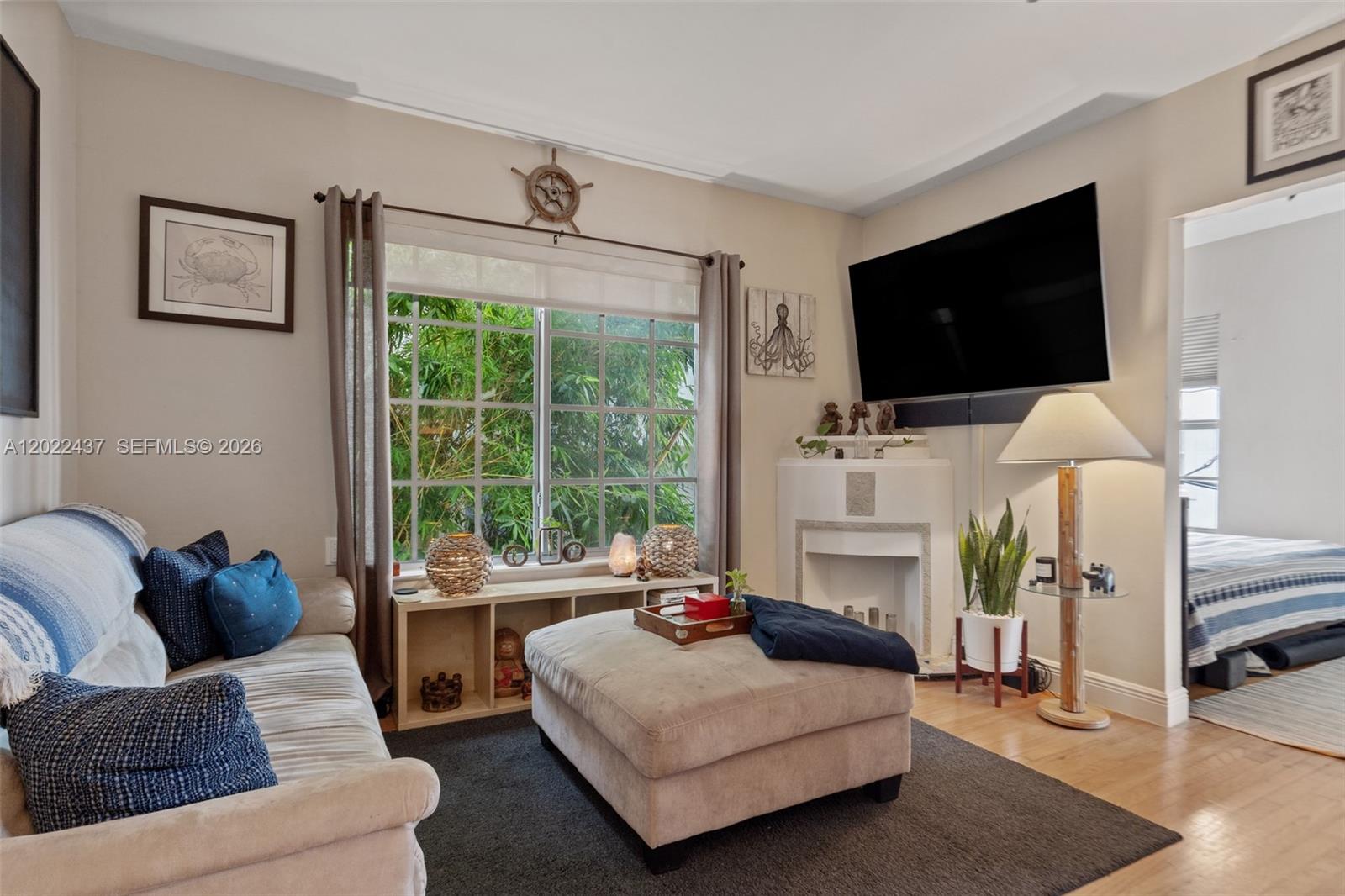 A living room features a beige sofa, ottoman, fireplace, wall-mounted television, and a large window — 936 Pennsylvania Ave # 205, Miami Beach FL 33139, MIAMI BEACH, FL