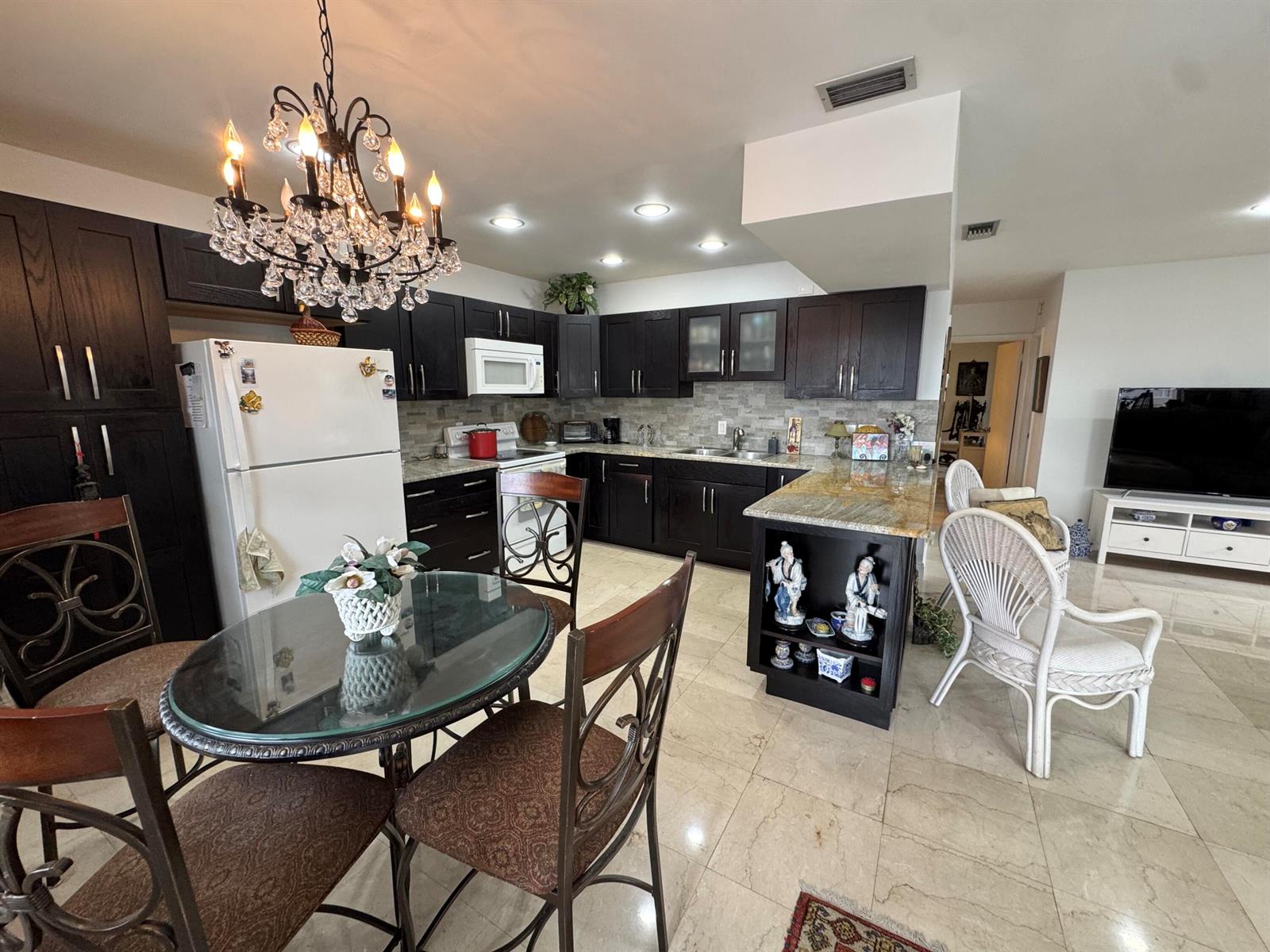 A kitchen with dark wood cabinets, granite countertops, a glass dining table, and tile flooring — 5505 N Ocean Boulevard # 203, Ocean Ridge FL 33435, OCEAN RIDGE, FL