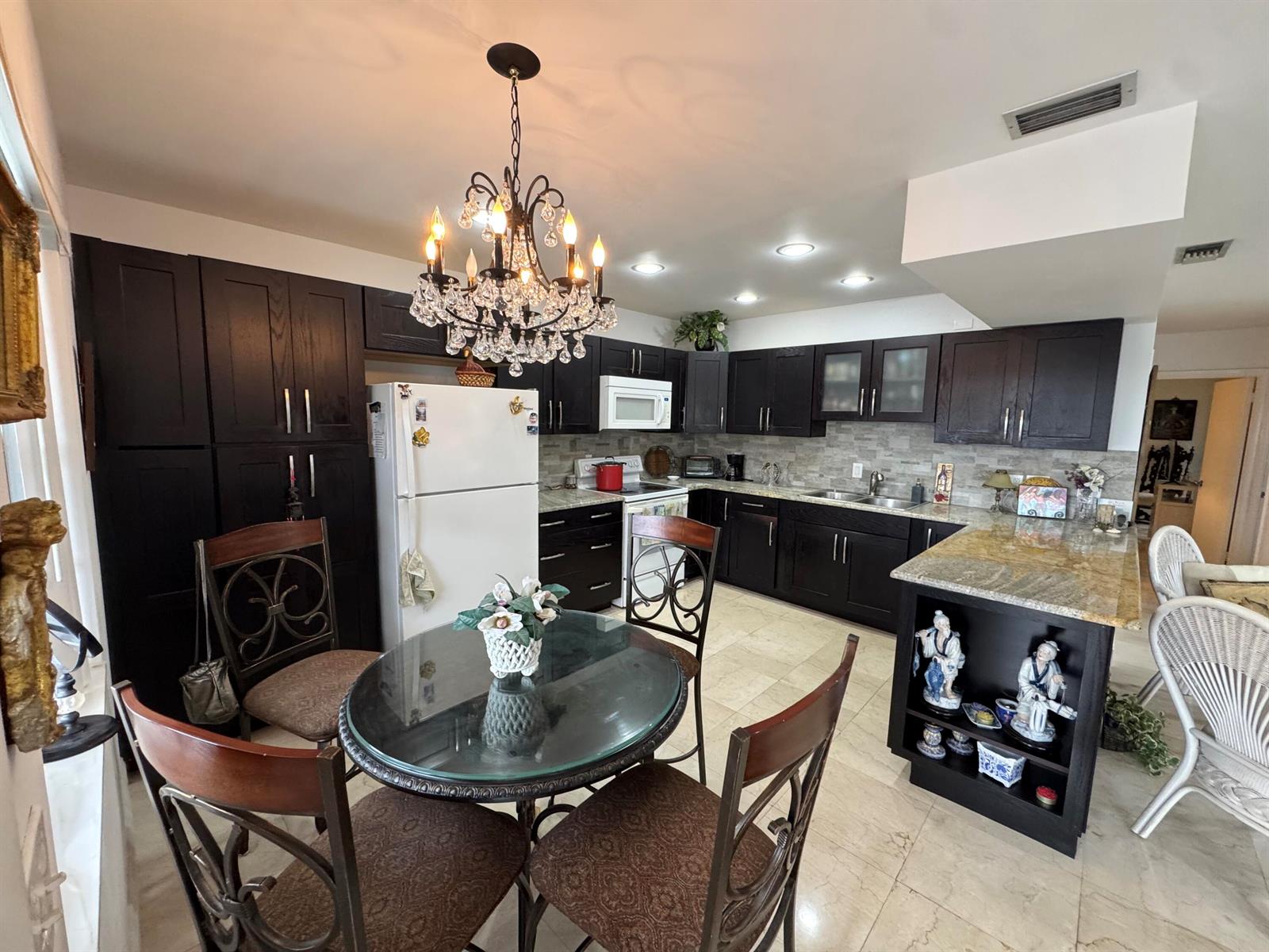 A kitchen with dark wood cabinets, granite countertops, a glass dining table, and a chandelier — 5505 N Ocean Boulevard # 203, Ocean Ridge FL 33435, OCEAN RIDGE, FL