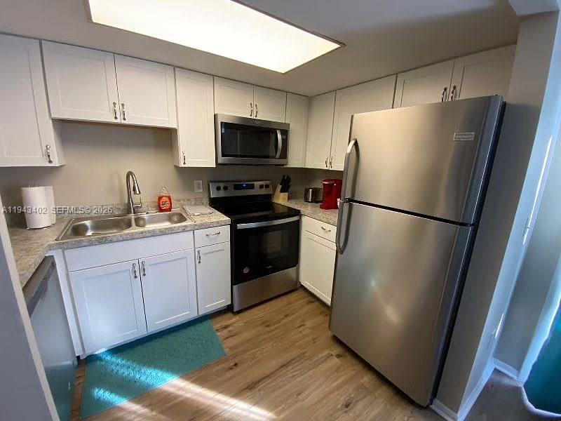 A kitchen features white cabinets, stainless steel appliances, and wood-look flooring — 6060 Village Cir, Orlando FL 32822, ORLANDO, FL