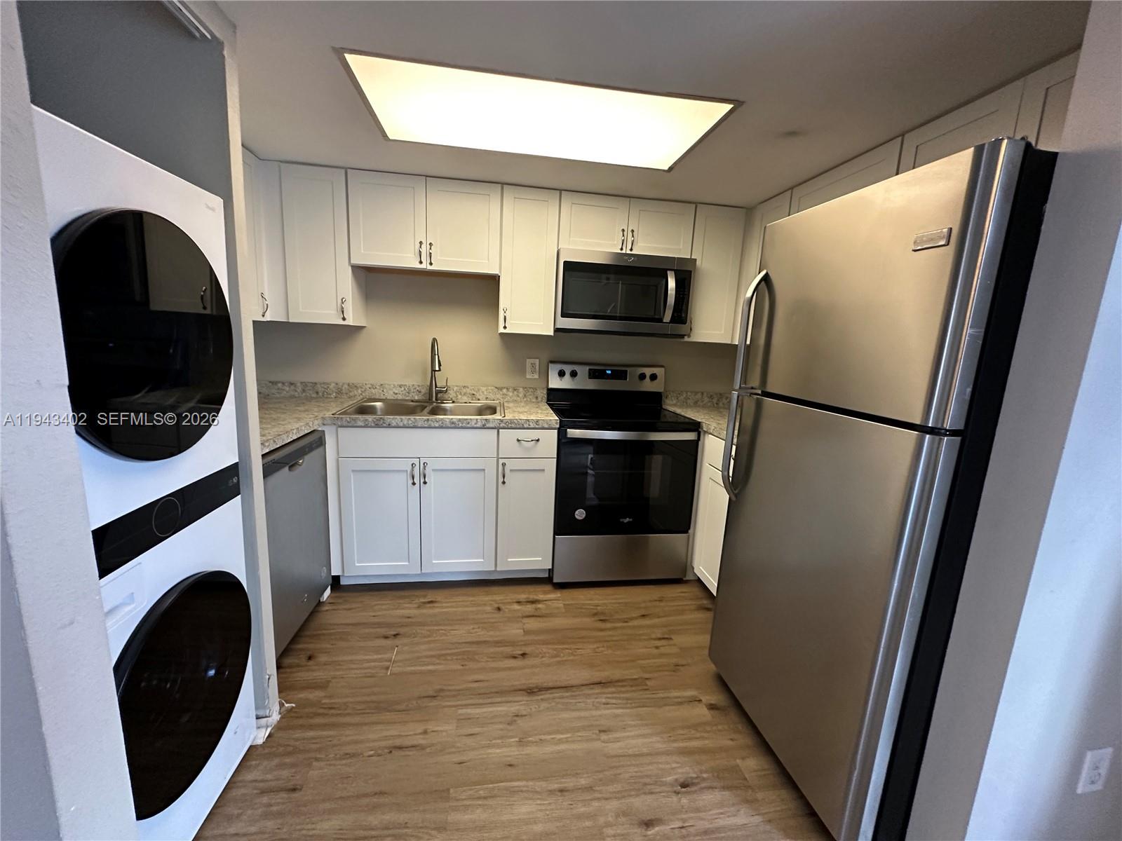 A kitchen features white cabinets, stainless steel appliances, a stacked washer-dryer, and wood-look flooring — 6060 Village Cir, Orlando FL 32822, ORLANDO, FL