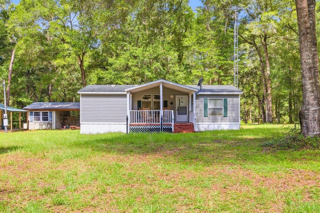 A single-story manufactured home with a front porch sits on a grassy, wooded lot — 9986 S FORESTLINE AVENUE, INVERNESS, FL