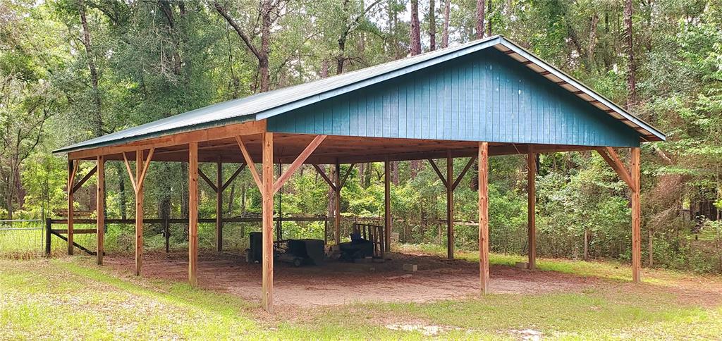 A large, open-sided wooden carport with a blue metal roof stands in a wooded area — 9986 S FORESTLINE AVENUE, INVERNESS, FL