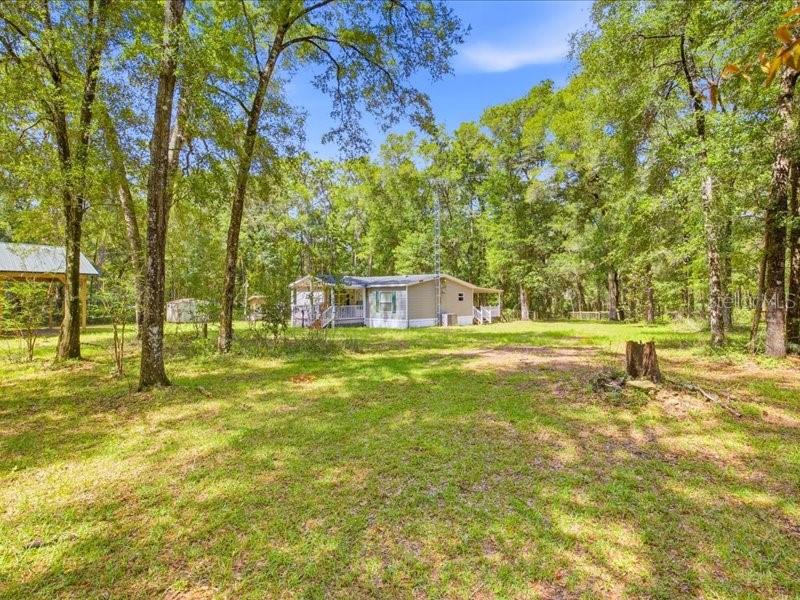 A single-story manufactured home sits in a grassy, wooded lot with a detached carport — 9986 S FORESTLINE AVENUE, INVERNESS, FL