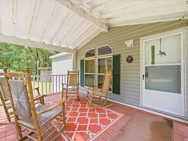 A covered wooden porch features three rocking chairs on a patterned orange rug — 9986 S FORESTLINE AVENUE, INVERNESS, FL