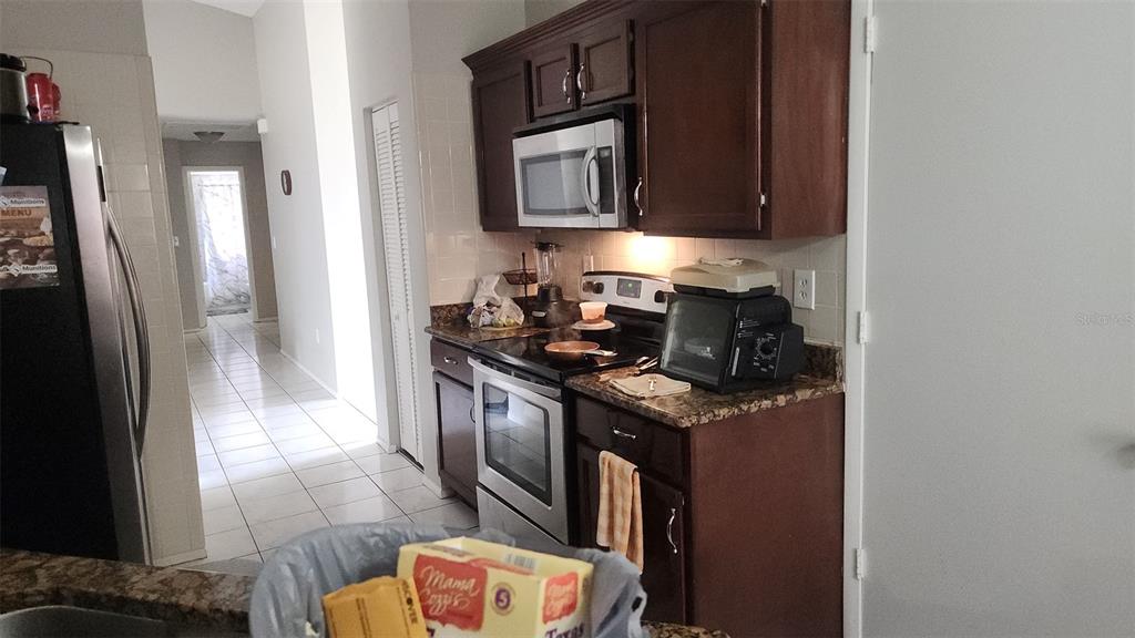 A kitchen features dark wood cabinets, granite countertops, stainless steel appliances, and tile flooring — 811 SAVONA PLACE, KISSIMMEE, FL