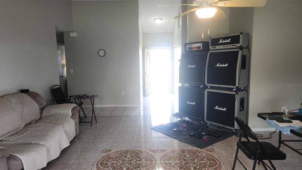 A living room features tile flooring, a beige sofa, and a large stack of Marshall amplifiers — 811 SAVONA PLACE, KISSIMMEE, FL