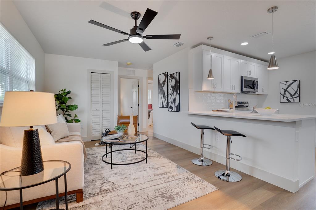 A modern open-concept living room and kitchen featuring white cabinetry, bar seating, and wood flooring — 4201 55TH AVENUE N, ST PETERSBURG, FL