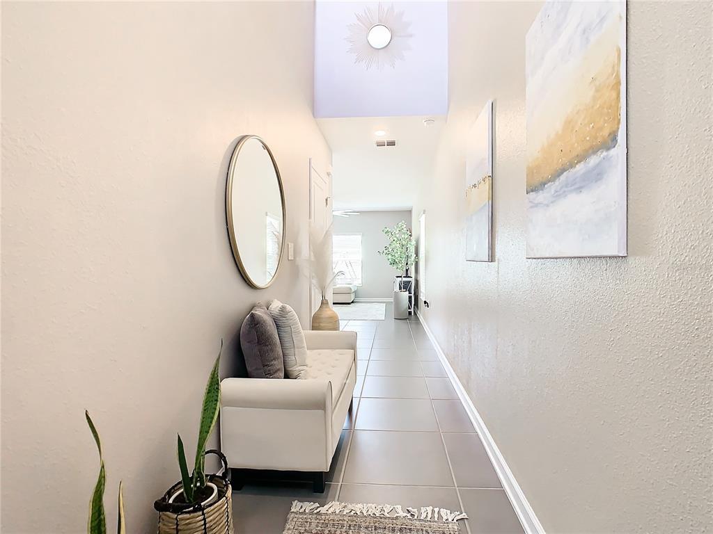 A hallway features light tile flooring, a white bench, wall art, and a round mirror — 1042 JOHN JACOB ROAD, DAVENPORT, FL