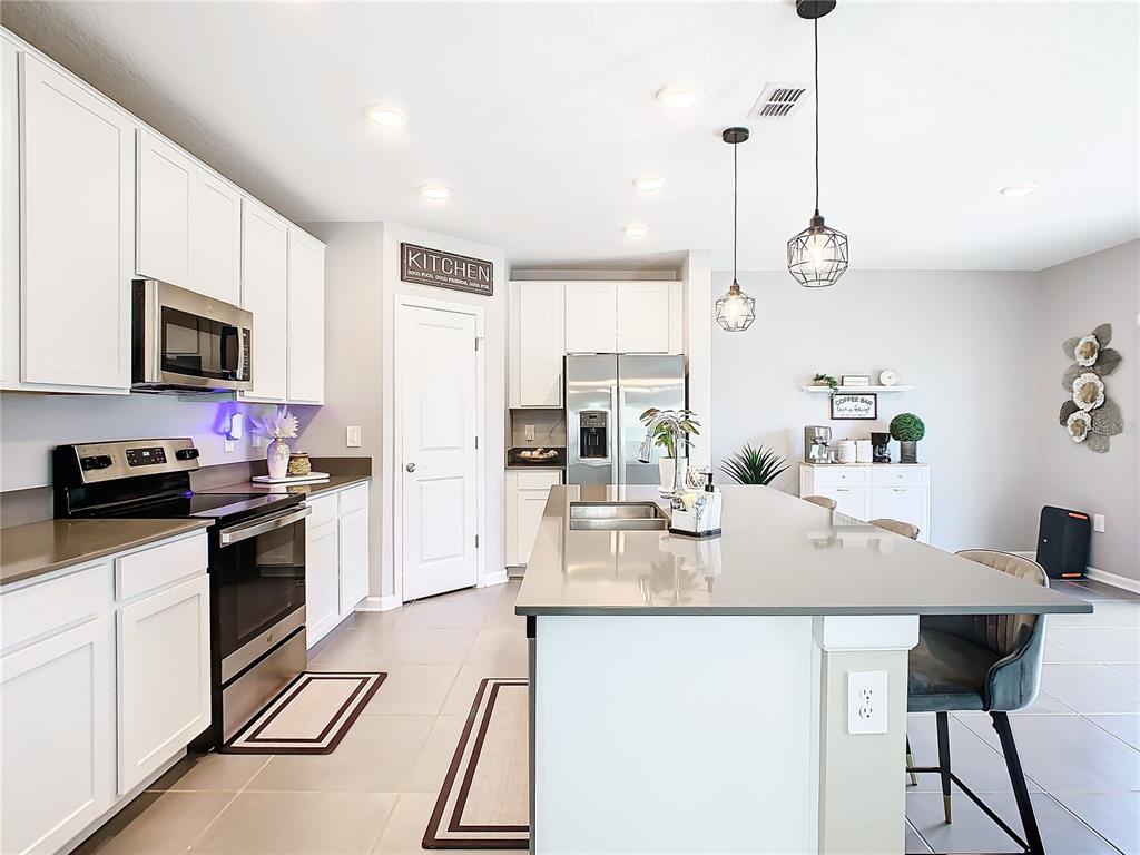 A modern kitchen features white cabinetry, stainless steel appliances, a large island, and tile flooring — 1042 JOHN JACOB ROAD, DAVENPORT, FL
