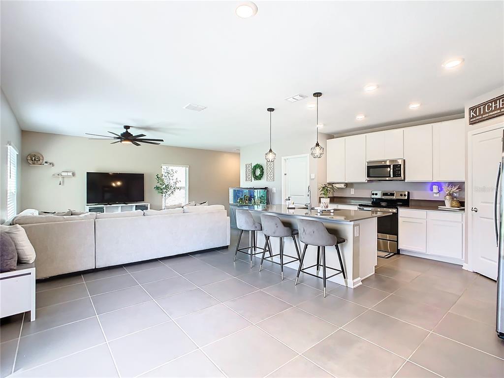 An open-concept living room and kitchen feature gray tile floors, white cabinetry, and a peninsula — 1042 JOHN JACOB ROAD, DAVENPORT, FL