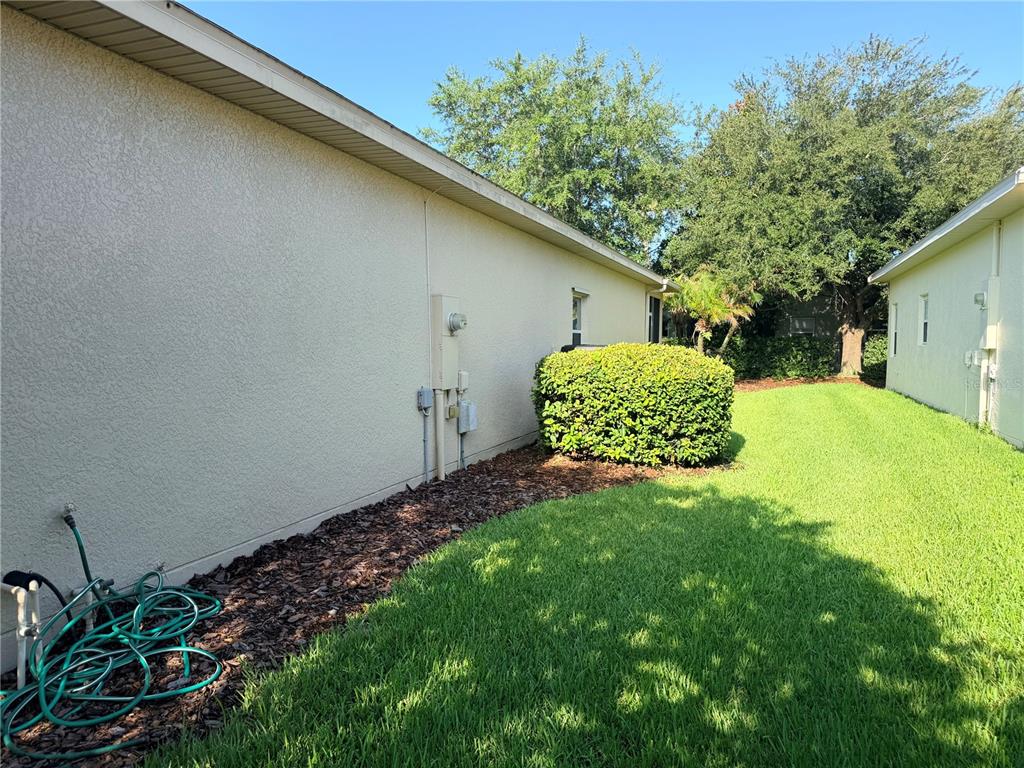 The side exterior of a house features a stucco wall, a garden bed, and lawn — 941 SHOREHAVEN DRIVE, KISSIMMEE, FL