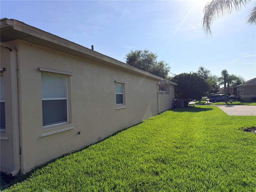 A side view of a beige stucco house exterior with two windows and a lawn — 941 SHOREHAVEN DRIVE, KISSIMMEE, FL