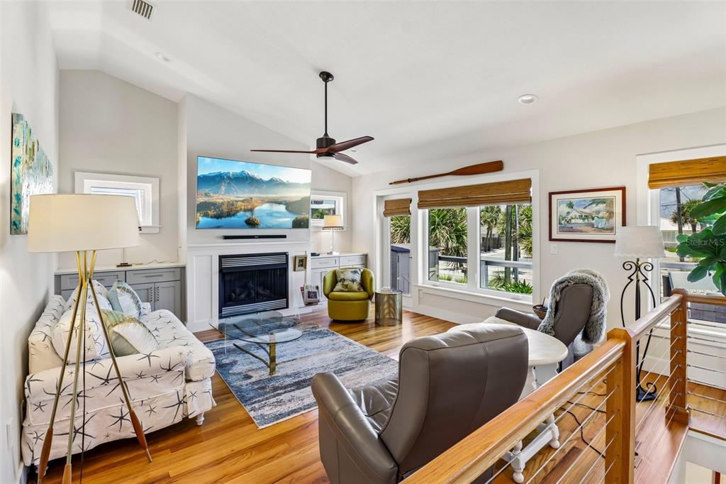A living room features a fireplace, a mounted television, hardwood floors, and a ceiling fan — 4730 VAN KLEECK DRIVE, NEW SMYRNA BEACH, FL
