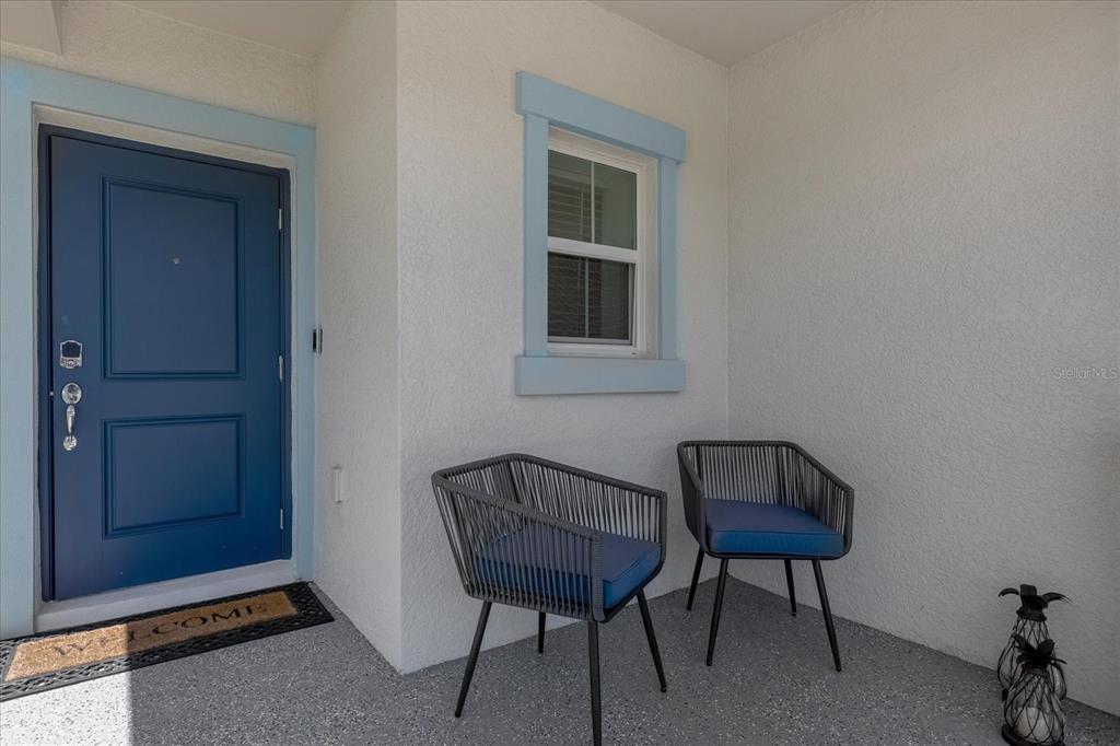 A covered porch features a blue front door, a window, and two modern patio chairs — 622 BELL PRAIRIE CIRCLE, LAKE WALES, FL