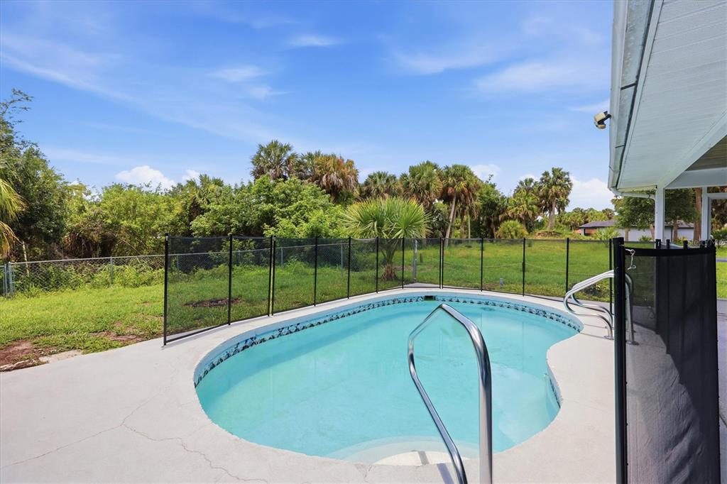 A backyard swimming pool with a safety fence and palm trees in the background — 4850 BRICKELL DRIVE, NORTH PORT, FL