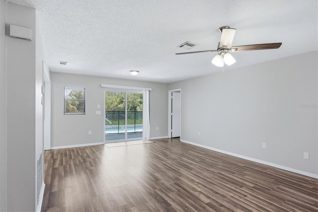 A living room with wood-look flooring, a ceiling fan, and sliding glass doors to a pool — 4850 BRICKELL DRIVE, NORTH PORT, FL