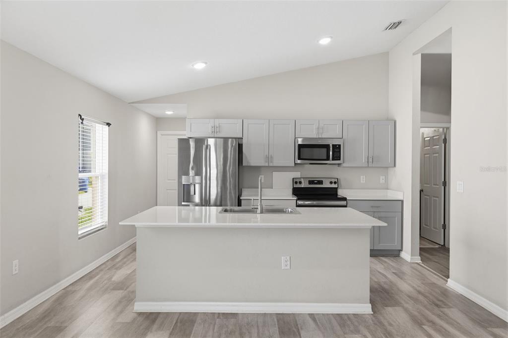 A kitchen with gray cabinets, stainless steel appliances, a white island, and light wood flooring — 13011 PENNYBROOK DRIVE, RIVERVIEW, FL