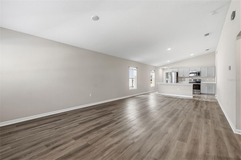 An open-concept living area features light gray walls, wood-look flooring, and a kitchen with cabinets — 13011 PENNYBROOK DRIVE, RIVERVIEW, FL