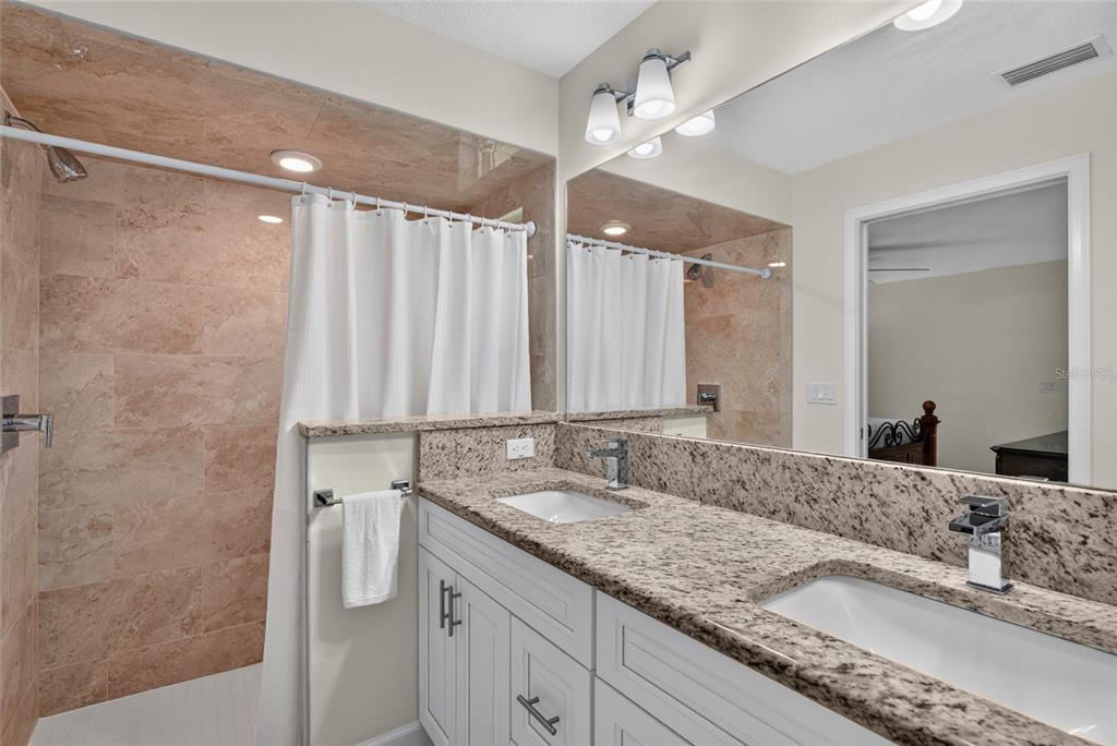 A bathroom features a double vanity with granite countertops, white cabinetry, and a tiled shower — 39 WHITE HOUSE DRIVE, PALM COAST, FL