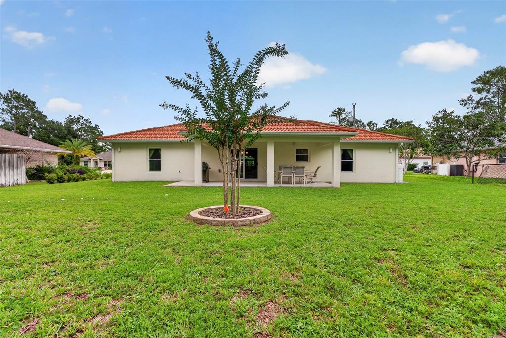 The backyard features a single-story house with a tiled roof, a patio, and a tree — 39 WHITE HOUSE DRIVE, PALM COAST, FL
