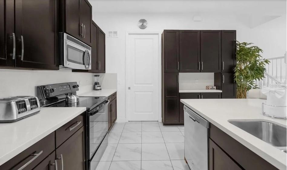A kitchen features dark wood cabinets, white countertops, stainless steel appliances, and white tile flooring — 450 CAPTIVA DRIVE, DAVENPORT, FL