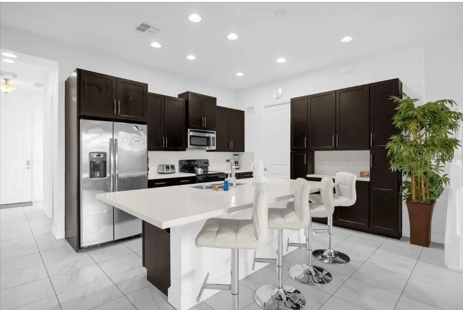 A modern kitchen features dark wood cabinets, white countertops, a central island, and tile flooring — 450 CAPTIVA DRIVE, DAVENPORT, FL