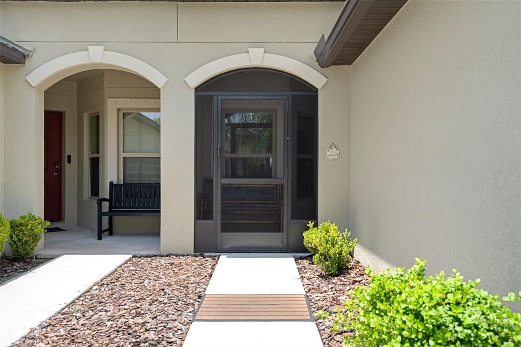 A beige stucco house exterior features two arched entryways, a screen door, and landscaping — 14055 WEDDINGTON TERRACE, HUDSON, FL