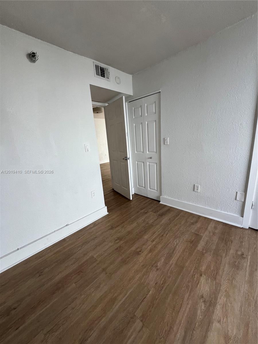 An empty room features light-colored walls, wood-look flooring, and a white interior door — NORTH BAY VILLAGE, FL