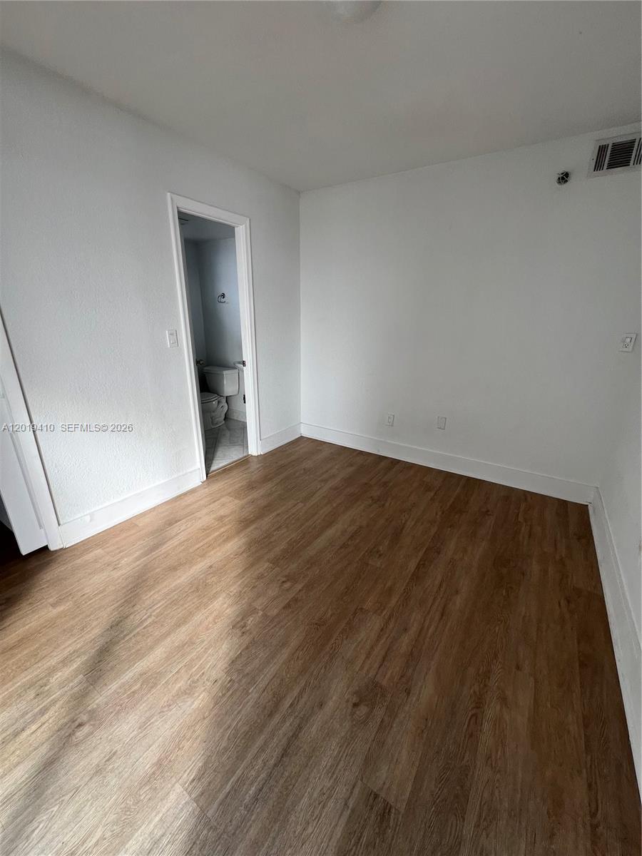 An empty room features white walls, wood-look flooring, and an open doorway to a bathroom — NORTH BAY VILLAGE, FL