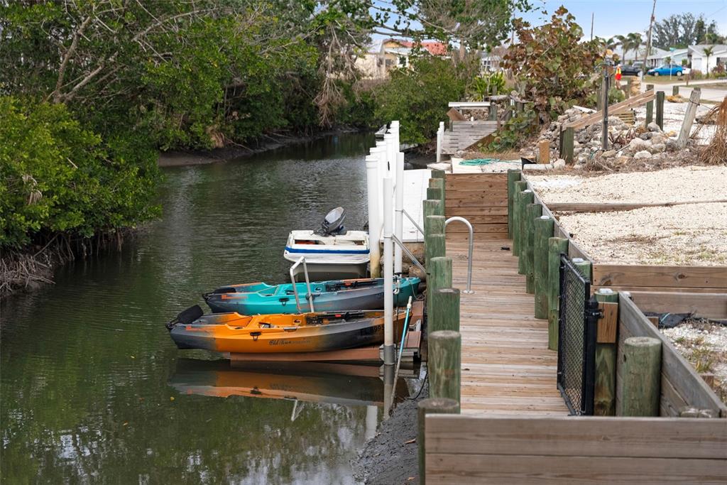 A wooden dock extends along a narrow canal with several kayaks and a small boat — 1845 EDISON DRIVE, ENGLEWOOD, FL
