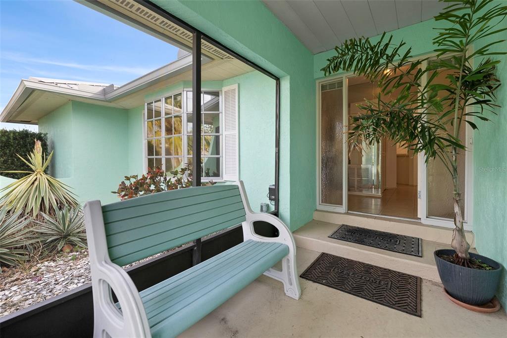 A light green covered porch features a bench, a potted plant, and a front entrance — 1845 EDISON DRIVE, ENGLEWOOD, FL
