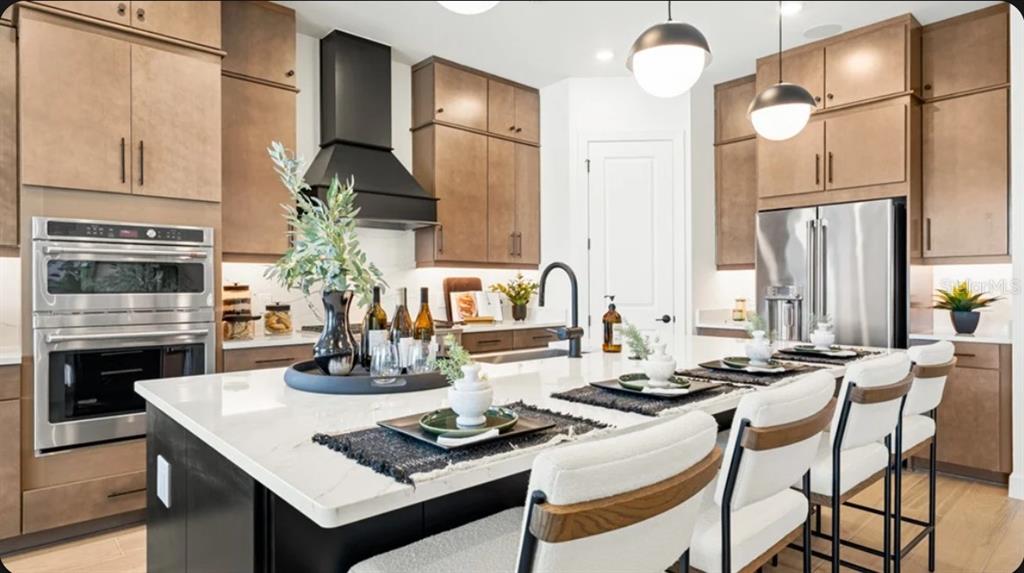 A modern kitchen features wood-toned cabinetry, a large white island, and a black range hood — 26625 DOVE DRIVE, PUNTA GORDA, FL