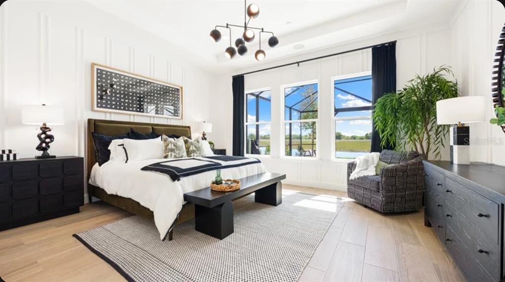 A modern bedroom features a king bed, black furniture, a chandelier, and large windows — 26625 DOVE DRIVE, PUNTA GORDA, FL