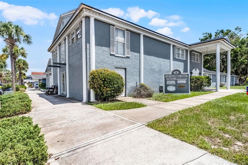 A two-story gray building with white columns and a covered entrance stands on a lawn — 131 W MAIN STREET, TAVARES, FL