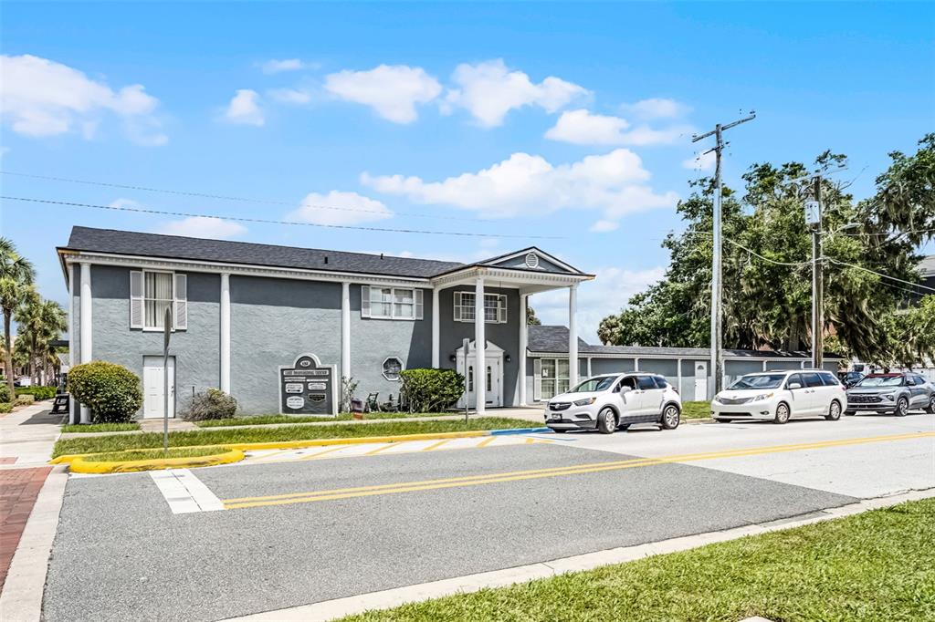 A two-story gray building with a white-columned entrance stands beside a street with parked cars — 131 W MAIN STREET, TAVARES, FL