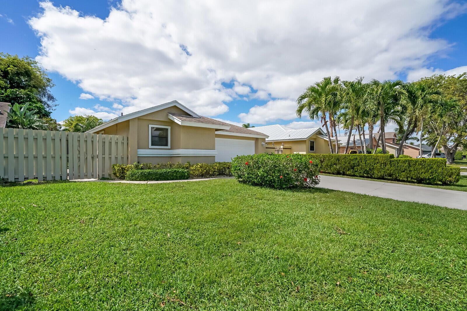 A tan single-story house with a white garage door, a fence, and a manicured lawn — 1080 NW 19th Terrace, Delray Beach FL 33445, DELRAY BEACH, FL