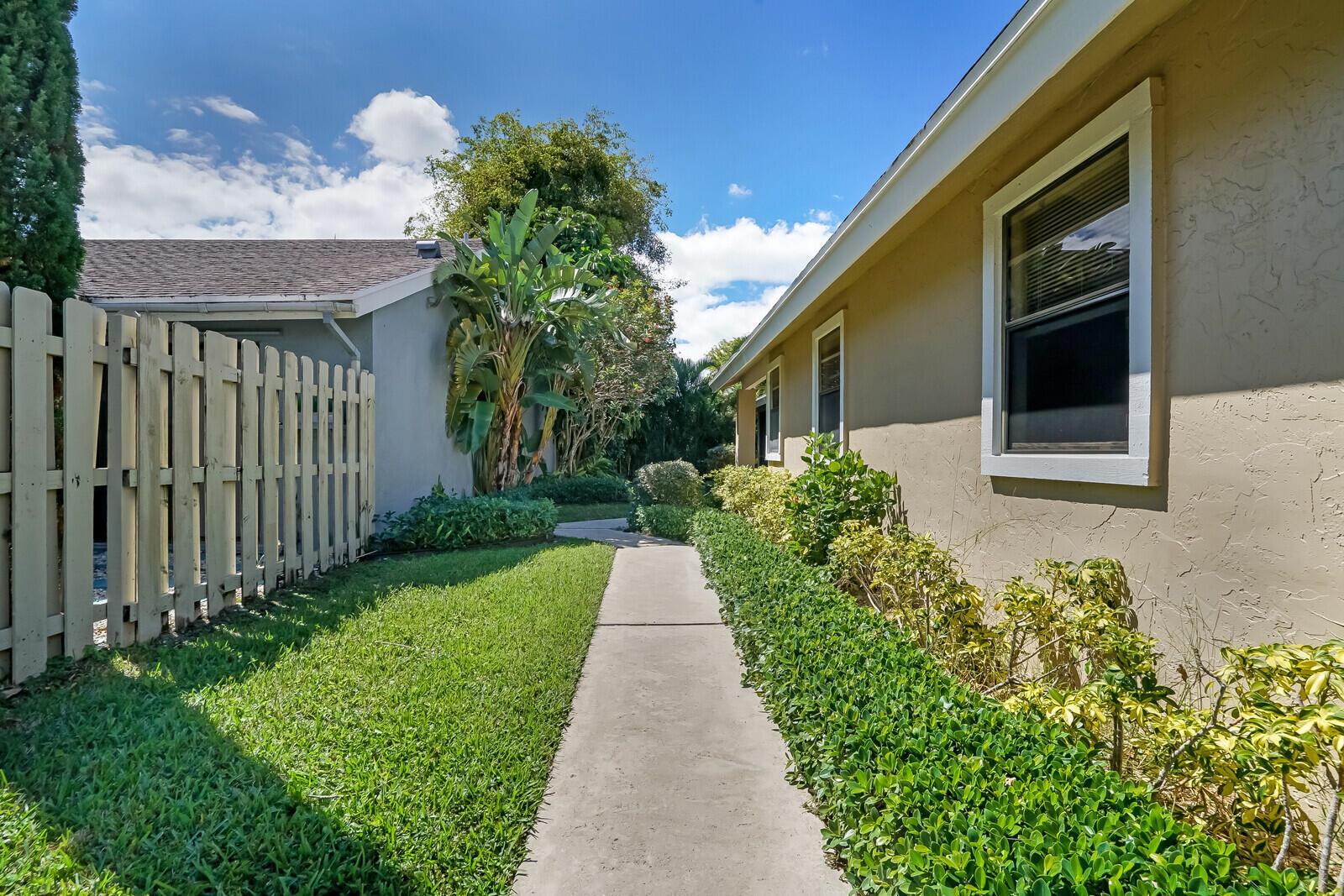 A concrete walkway leads between a wooden fence and a tan house with landscaping — 1080 NW 19th Terrace, Delray Beach FL 33445, DELRAY BEACH, FL