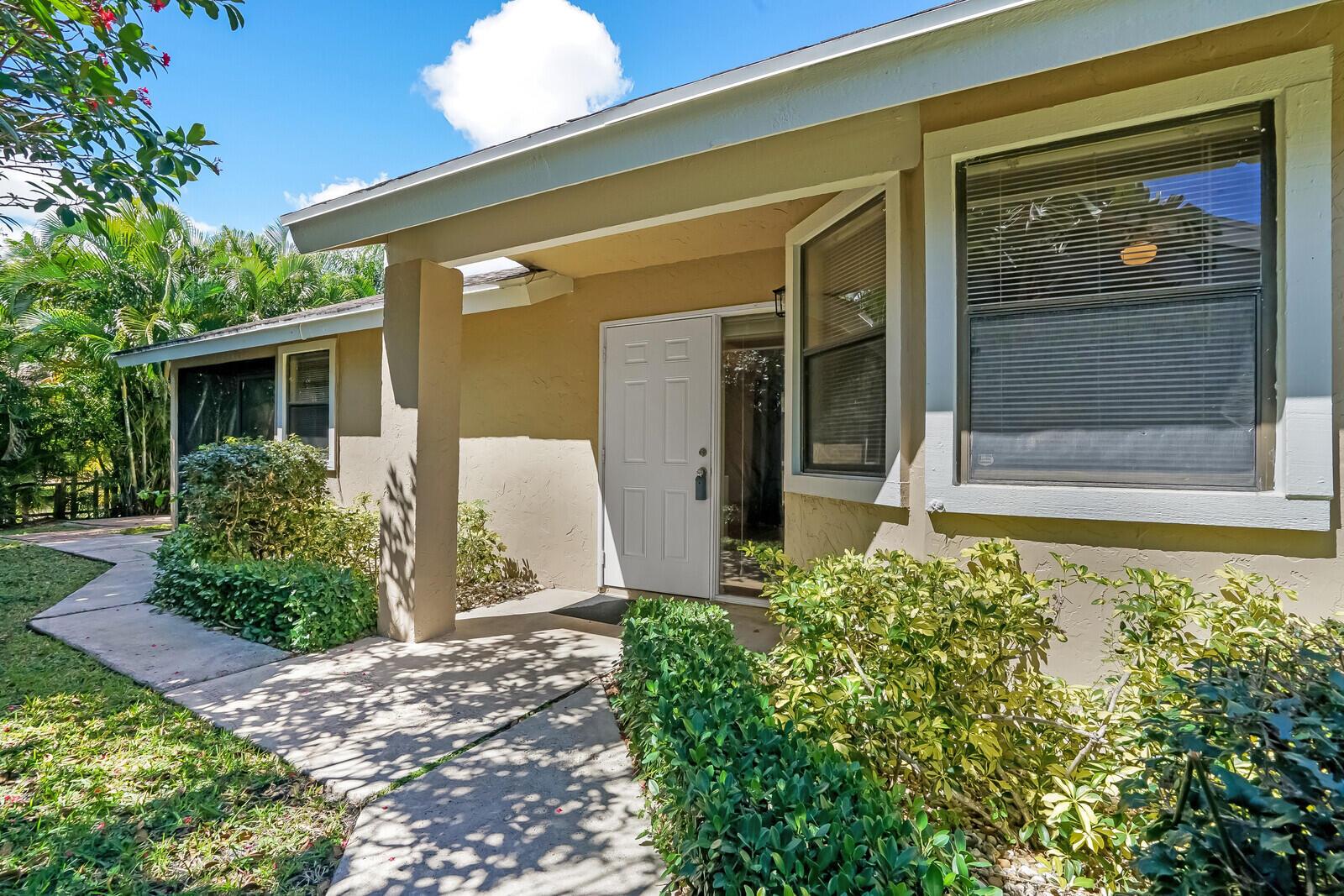 The exterior of a tan house features a white front door and a concrete walkway — 1080 NW 19th Terrace, Delray Beach FL 33445, DELRAY BEACH, FL