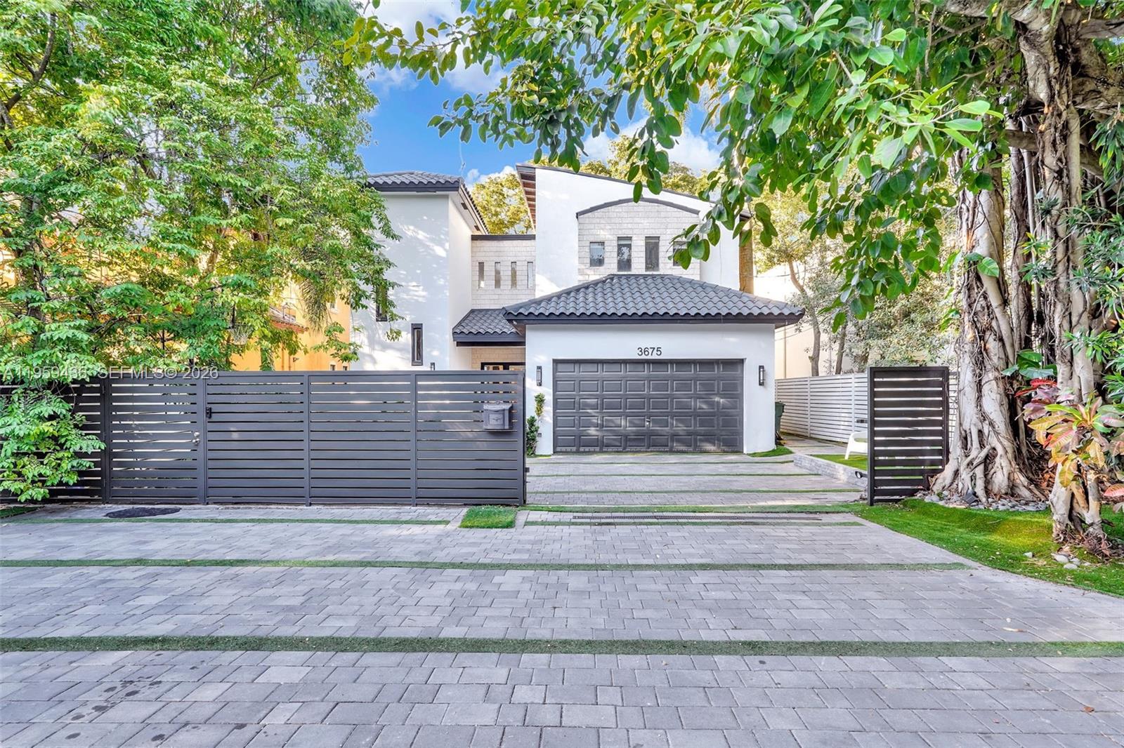 A modern two-story house features a dark garage door, paved driveway, and horizontal privacy fencing — 3675 Loquat Ave, Miami FL 33133, MIAMI, FL